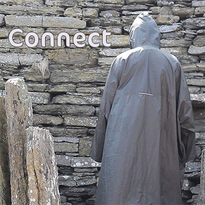 back view of a man in a rain cape in front of a stone wall